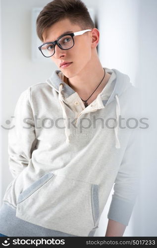 Portrait of young fashionable man leaning on white wall and wearing glasses. He is trendy fashionable or maybe gay