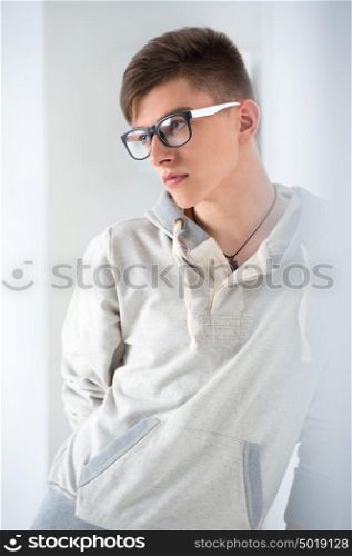 Portrait of young fashionable man leaning on white wall and wearing glasses. He is trendy fashionable or maybe gay