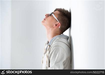 Portrait of young fashionable man leaning on white wall and wearing glasses. He is trendy fashionable or maybe gay