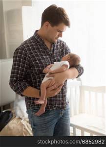 Portrait of young father holding newborn baby on hands at home