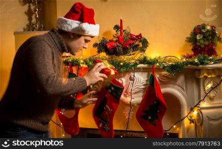 Portrait of young father putting gifts in Christmas stockings at fireplace