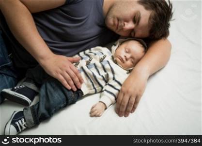 Portrait of young father sleeping on bed with newborn baby boy