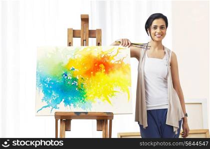 Portrait of young female artist standing by painting