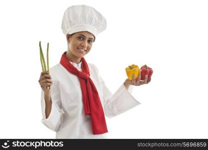Portrait of young female chef holding capsicums and asparagus isolated over white background