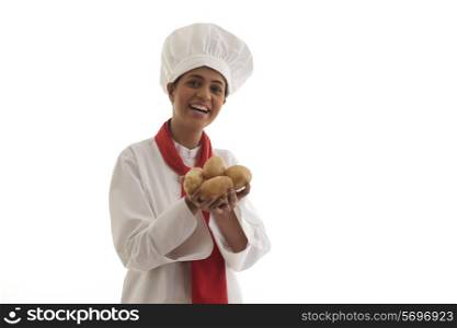 Portrait of young female chef holding potatoes while laughing over white background