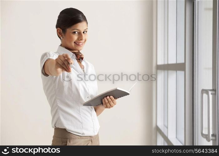 Portrait of young female executive giving pen to write in diary