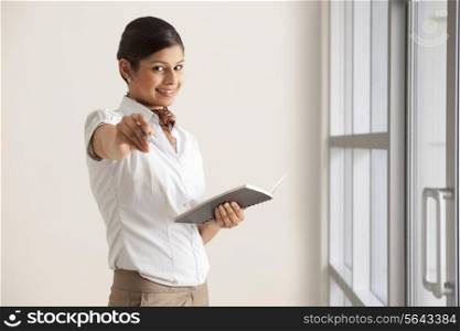 Portrait of young female executive giving pen to write in diary