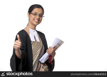 Portrait of young female lawyer showing thumbs up sign while holding documents against white background