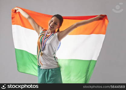 Portrait of young female medalist celebrating victory with Indian flag isolated over gray background