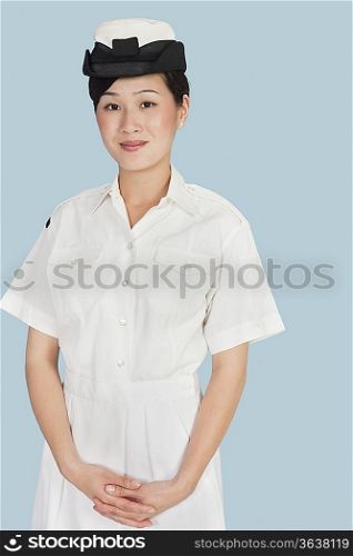 Portrait of young female Navy officer with hands clasped standing over light blue background