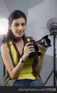 Portrait of young female photographer with camera sitting in studio
