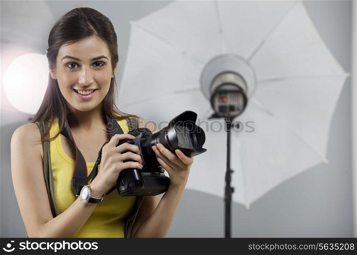 Portrait of young female photographer with digital camera in studio