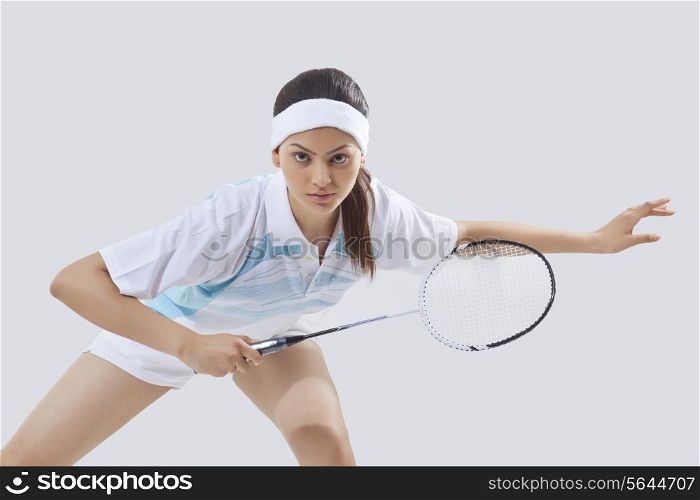 Portrait of young female player playing badminton isolated over gray background