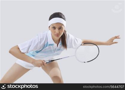 Portrait of young female player playing badminton isolated over gray background