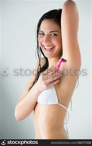Portrait of young female shaving her armpit in bathroom under shower, water is splashing around