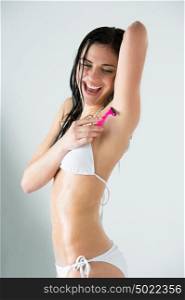 Portrait of young female shaving her armpit in bathroom under shower, water is splashing around