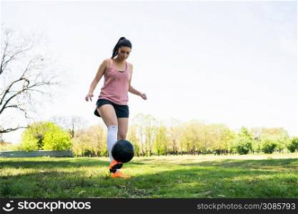 Portrait of young female soccer player running around cones while practicing with ball on field. Sports concept.