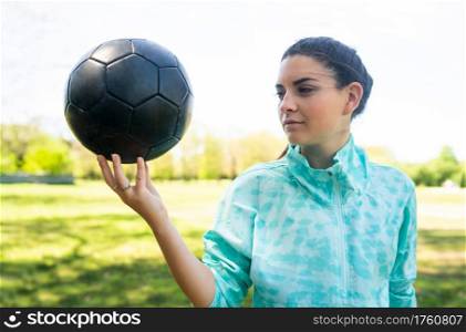 Portrait of young female soccer player standing on field and holding football ball. Sports concept.