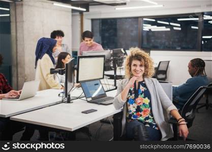 portrait of young female software developer at busy startup office with her multiethnic business team in background