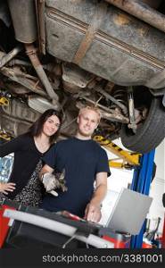 Portrait of young female standing with mechanic using laptop in auto repair shop