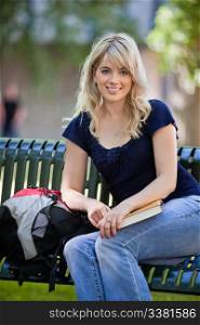 Portrait of young female student sitting on bench at college campus