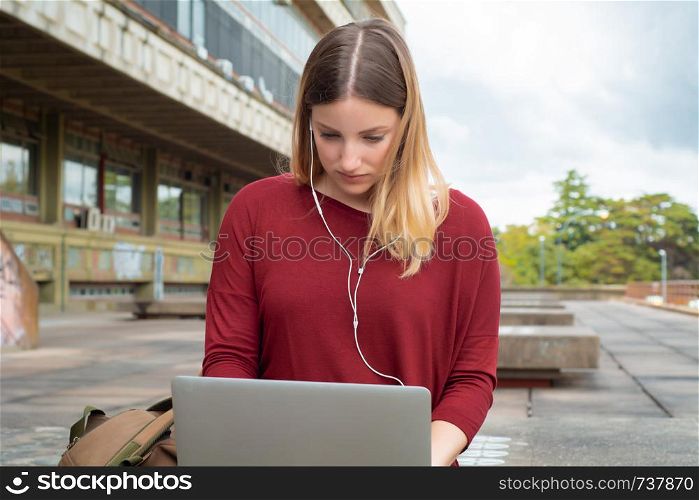Portrait of young female student using laptop computer outdoors. Education concept