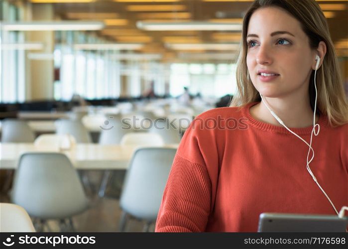 Portrait of young female student with earphones using digital tablet in the university library.