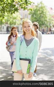Portrait of young female student with friends in background on street