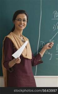 Portrait of young female teacher explaining a lesson while standing against chalkboard