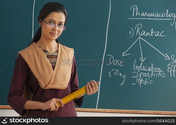 Portrait of young female teacher holding ruler against chalkboard