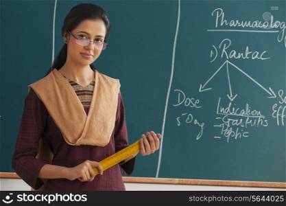 Portrait of young female teacher holding ruler against chalkboard