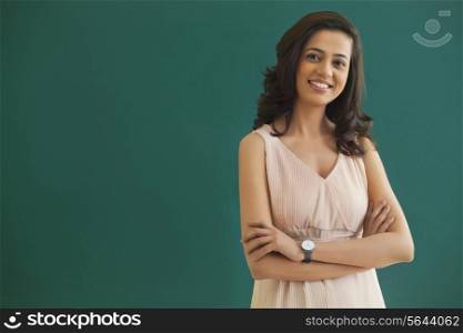 Portrait of young female teacher with arms crossed standing against green board