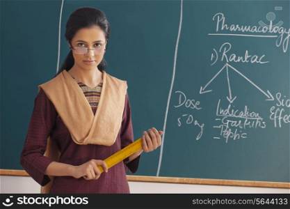 Portrait of young female teacher with attitude holding ruler against chalkboard