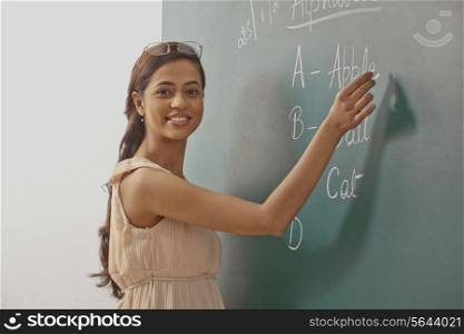 Portrait of young female teacher writing on green board