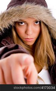 portrait of young female with winter coat pointing at camera on an isolated background