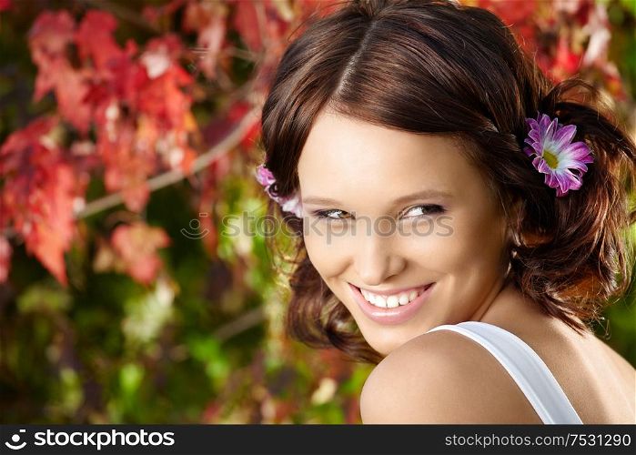 Portrait of young flirting woman against red leaves in a summer garden