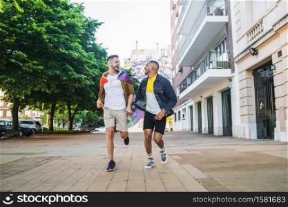 Portrait of young gay couple holding their hands and running together with rainbow flag in the street. LGBT and love concept.