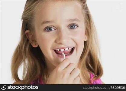 Portrait of young girl flossing teeth against gray background