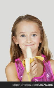 Portrait of young girl holding banana against gray background