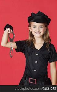 Portrait of young girl in police costume holding handcuffs against red background