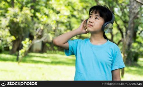 Portrait of young girl listens to music with modern headphones in park outdoors. Preteen girl enjoying rhythms in listening to music with headphones wireless