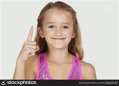 Portrait of young girl pointing upwards against gray background