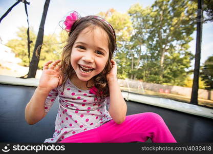 Portrait of young girl sitting on large trampoline, laughing