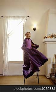 Portrait of young girl standing on chair swinging long cape