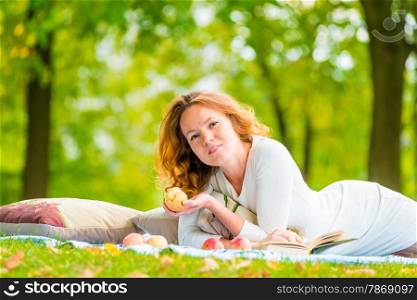 portrait of young girl with books and apple on the plaid in the park