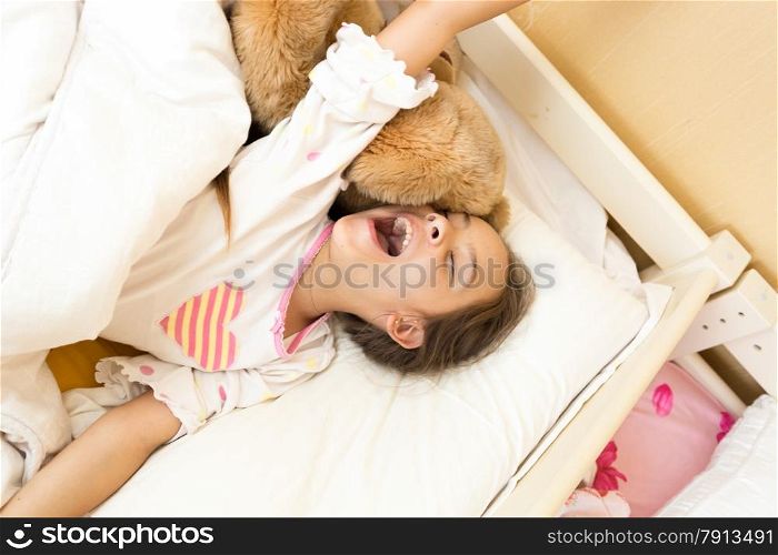 Portrait of young girl yawning in bed and stretching hands