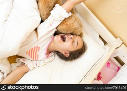 Portrait of young girl yawning in bed and stretching hands