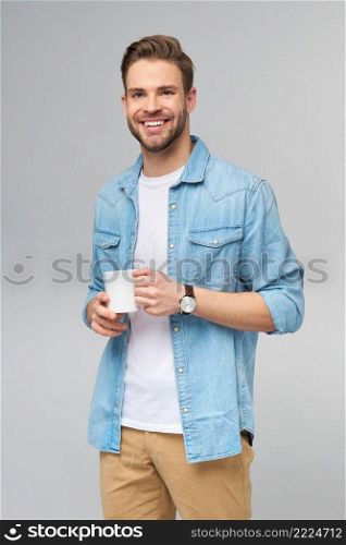 Portrait of young handsome caucasian man in jeans shirt over light background holding cup of coffee.. Portrait of young handsome caucasian man in jeans shirt over light background holding cup of coffee