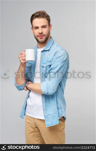 Portrait of young handsome caucasian man in jeans shirt over light background holding cup of coffee.. Portrait of young handsome caucasian man in jeans shirt over light background holding cup of coffee
