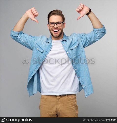 Portrait of young handsome caucasian man in jeans shirt showing at himself by big thumbs standing over light background.. Portrait of young handsome caucasian man in jeans shirt showing at himself by big thumbs standing over light background